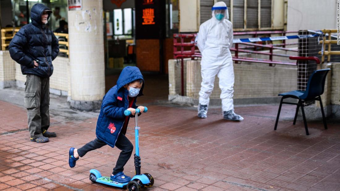 A child rides a scooter past a police officer wearing protective gear outside the Hong Mei House in Hong Kong on February 11. More than 100 people evacuated the housing block after four residents in two different apartments tested positive for the coronavirus.